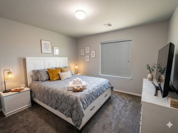 A bedroom with a bed, bedside tables, a TV, and a window with blinds.