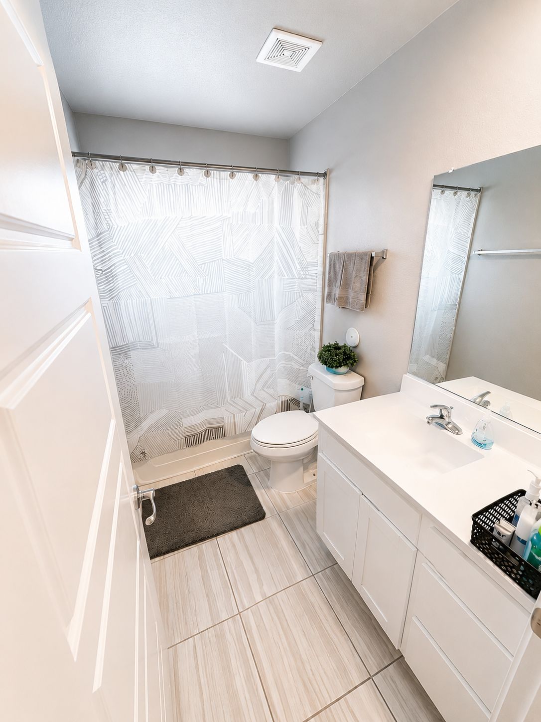 A modern bathroom with a shower curtain, toilet, sink, and a mirror.