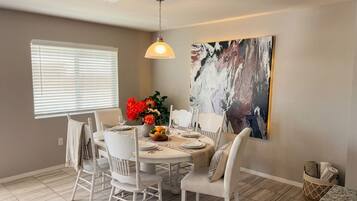 A dining area with a round table, white chairs, and a hanging light fixture.