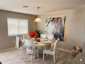 A dining area with a round table, white chairs, and a hanging light fixture. - Flexible 4BR Estate: Main Villa & Private Suites (Socorro)