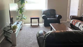 A living room with a ceiling fan, a sofa, a chair, a coffee table, a TV, and a plant.