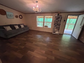 A living room with a grey sofa, wooden flooring, a chandelier, a bookshelf, and a sliding glass door leading to a balcony. - 4 Bedrooms In Nature Only 35 Min. to Gatlinburg (Cosby)