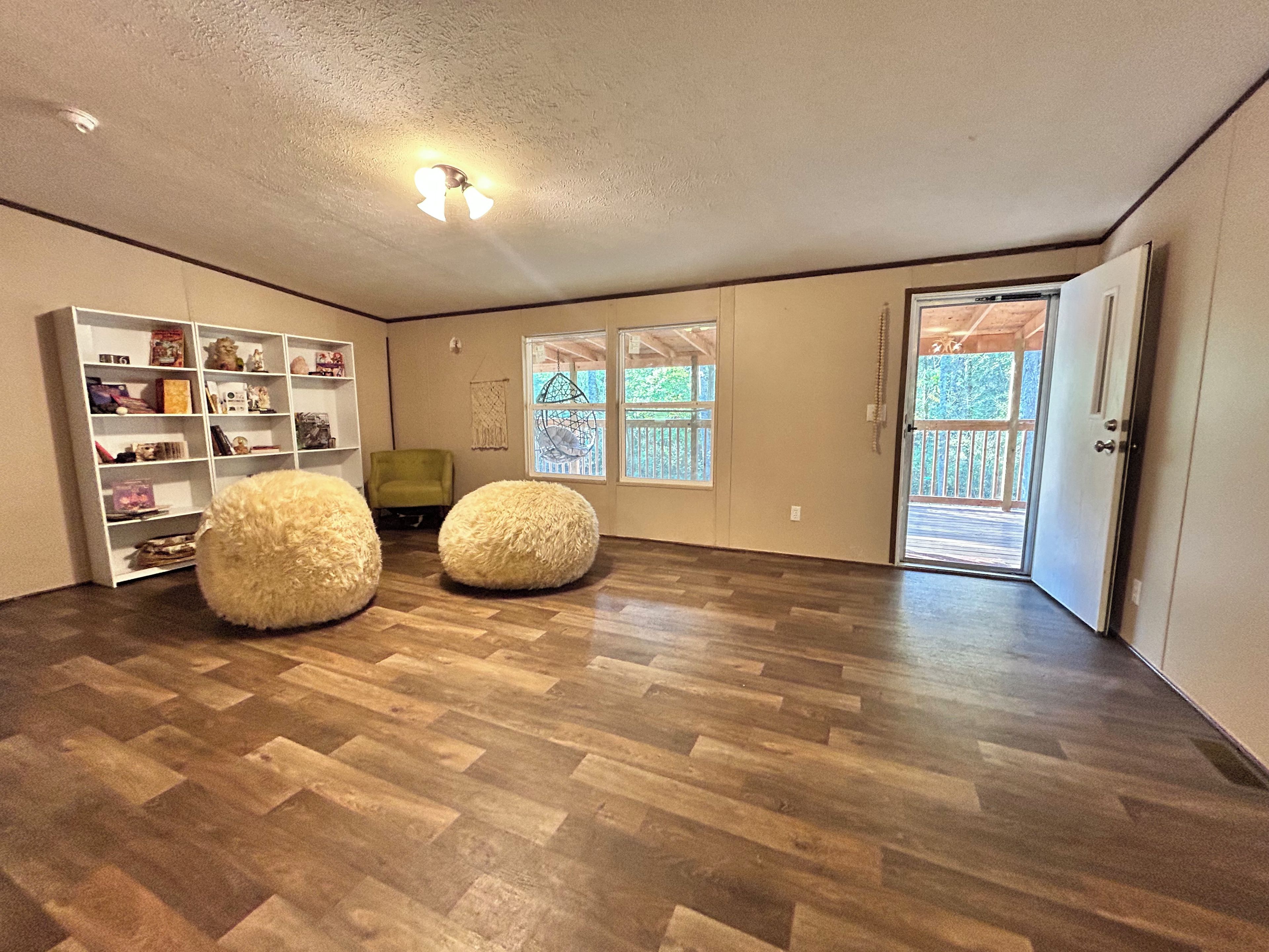 A spacious room with a wooden floor, a white bookshelf, two round bean bag chairs, and a door leading to an outdoor area.