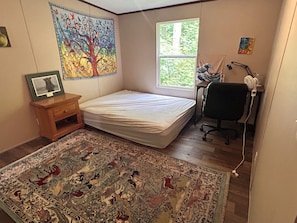 Ein Schlafzimmer mit Bett, Schreibtisch, Stuhl, Fenster, Teppich und Wandbild.