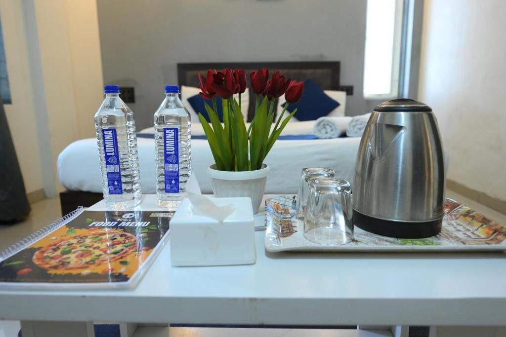 Habitació d'hotel amb un llit, una taula de nit amb una ampolla d'aigua, un vas amb flors vermelles, una cafetera i un menú de menjars.