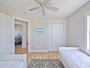 Ein Schlafzimmer mit zwei Betten, einem Deckenventilator, einer Tür zu einem weiteren Zimmer und einem Bild an der Wand.