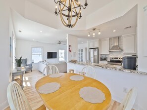 A modern kitchen with white cabinetry, a central island, and a dining area with a wooden table and chairs. - Harbor-View Condo w/ Sun Deck near Cape May (Cape May)