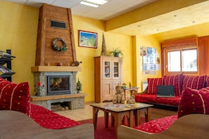 A cozy living room with a fireplace, red upholstered seating, and a wooden cabinet. - Domaine skiable | Au pied du télésiège | Piscine (La Toussuire)