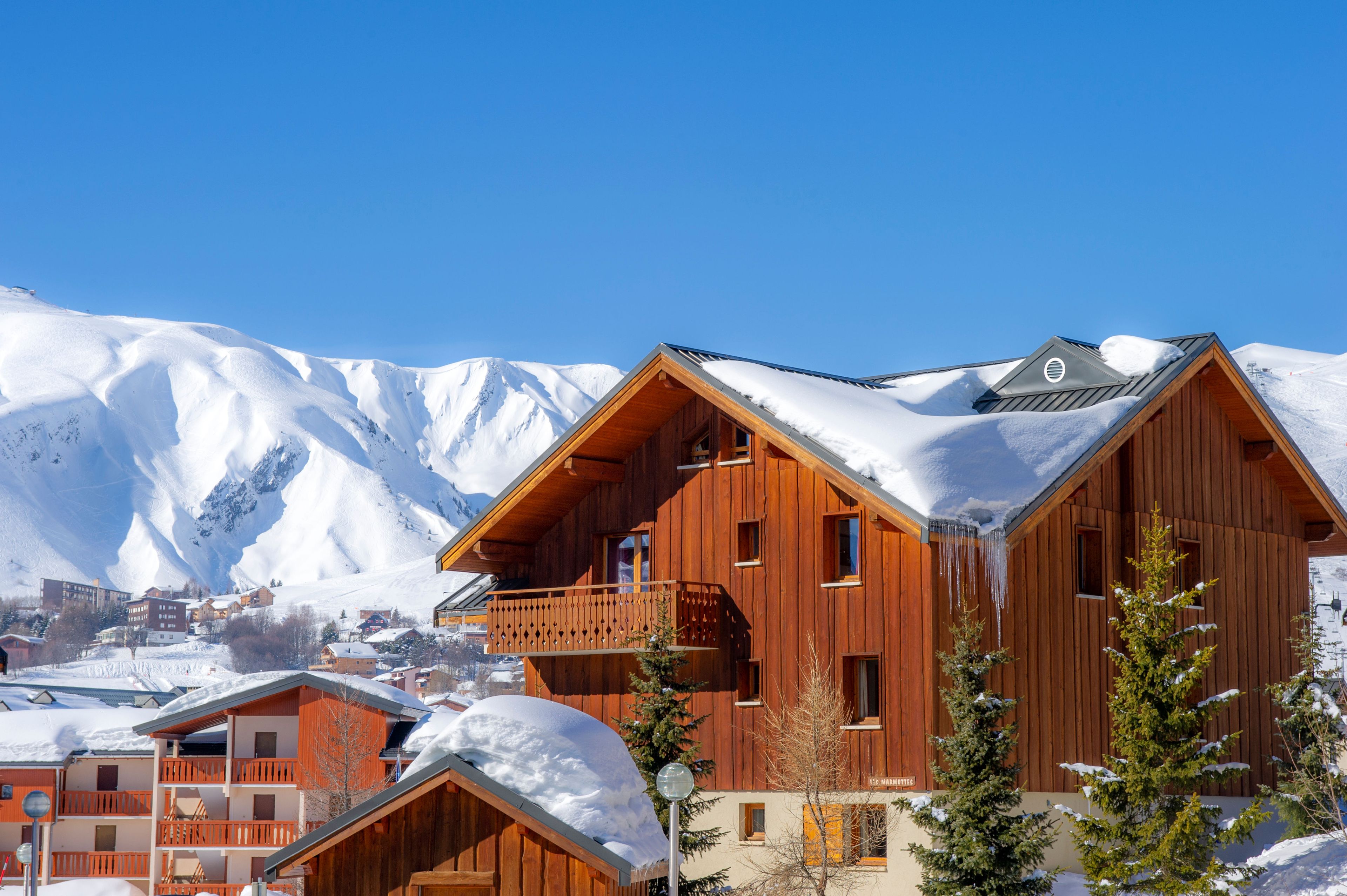 Un chalet en bois doté d’un balcon, entouré de montagnes enneigées.