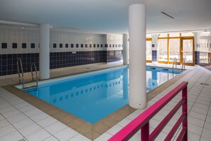 An indoor swimming pool with clear blue water, surrounded by white and black tiled walls, and a pink safety railing. - Au cœur du Parc de la Vanoise | Piscine sur place (Pralognan-la-Vanoise)