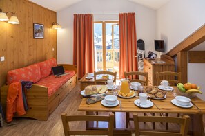 A cozy room with a wooden sofa, a dining table set with breakfast, and a view of a snowy landscape through the window. - Au cœur du Parc de la Vanoise | Piscine sur place (Pralognan-la-Vanoise)