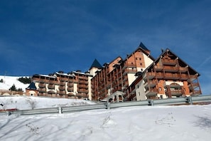 Ein mehrstöckiges Hotel mit Balkonen, im Hintergrund eine Skipiste und ein klarer Himmel.