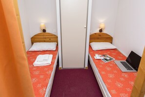 A small, narrow room with two single beds, each with a wooden headboard, white pillows, and a red patterned bedspread. There is a door in the center, and a laptop is placed on one of the beds. - T2 à l’entrée de la station | Piscine couverte (Pralognan-la-Vanoise)