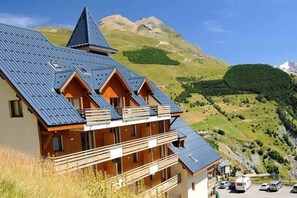 A mountain lodge with multiple balconies, a steep roof, and a view of the surrounding hills. - Télécabine Super Venosc à 2 pas | Station sportive (Les Deux Alpes)
