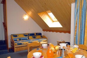 A dining area with a table set for breakfast, a sofa, and a skylight. - Télécabine Super Venosc à 2 pas | Station sportive (Les Deux Alpes)