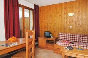 A room with a wooden wall, a sofa, a table with a bowl of fruit, and a television. - Télécabine "Super Venosc" au pied de la résidence (Les Deux Alpes)