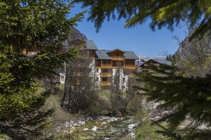 A lodge with multiple balconies overlooking a river, surrounded by trees and mountains.