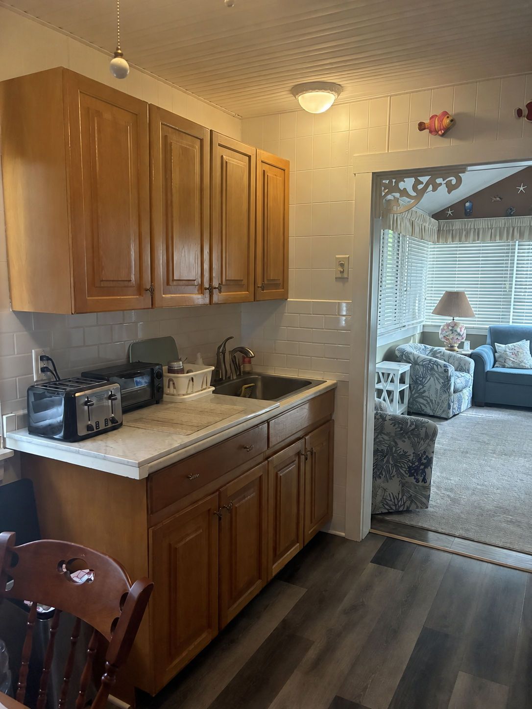 A compact kitchen with wooden cabinets, a countertop, and a dining area with a chair.