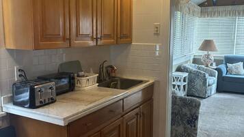 A compact kitchen with wooden cabinets, a countertop, and a dining area with a chair.