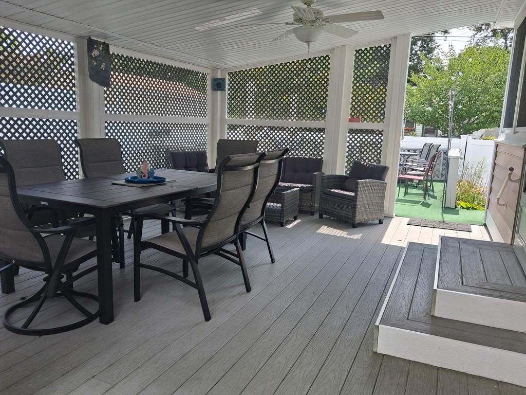 An outdoor patio with a table and chairs, a ceiling fan, and a view of the backyard.