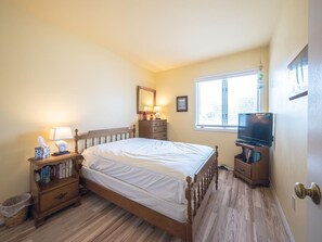 Ein Schlafzimmer mit einem hölzernen Bett, Nachttischen, einem Fernseher, einem Fenster und einer Tür.