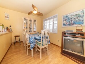 Un'area pranzo con un tavolo apparecchiato per due, una ventola a soffitto, una finestra con vista e un televisore su un supporto.