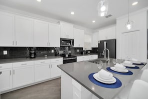 A modern kitchen with white cabinetry, a central island, and a dining area with blue placemats. - EV_9085 - 5 Bed 5 Bath Villa with Private Pool with Spillover Spa, Custom Games (Davenport)