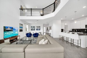 A spacious living area with a high ceiling, a balcony, and a modern kitchen with bar seating. - EV_9085 - 5 Bed 5 Bath Villa with Private Pool with Spillover Spa, Custom Games (Davenport)
