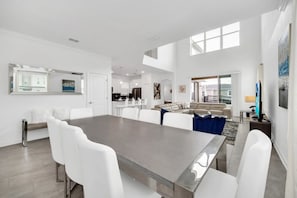 A spacious living area with a large dining table, white furniture, and a kitchen in the background. - EV_9085 - 5 Bed 5 Bath Villa with Private Pool with Spillover Spa, Custom Games (Davenport)