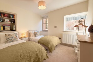 Une chambre avec deux lits, une bibliothèque, un radiateur et une fenêtre.