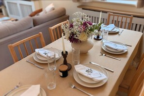 Une table à manger dressée avec des assiettes, des couverts, des verres et un centre de table agrémenté de fleurs.