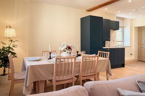 A dining area with a table set for four, wooden chairs, a vase with flowers, and a lamp. - Entire Home in Moreton-in-Marsh (Moreton-in-Marsh)