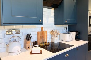 Une cuisine moderne avec des meubles bleus, un plan de travail blanc et divers appareils, notamment une bouilloire, un grille-pain et une machine à café.