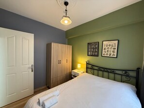 Ein Schlafzimmer mit einem Bett, einem Kleiderschrank, einem Nachttisch mit Lampe und zwei gerahmten Pflanzenbildern an der Wand.