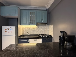 Eine Küche mit türkis-blauen Schränken, einem Gasherd, einem Kühlschrank und einer Kaffeemaschine.