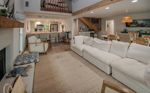 Ein geräumiger Wohnbereich mit einem weißen Sofa, einem Couchtisch und einem Kamin. Im Hintergrund ist eine Küche mit modernen Geräten zu sehen.