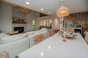A modern living room with a fireplace, white sofas, a dining table with a decorative centerpiece, and a kitchen in the background. - Santa Clara: Modern 3BR Harborfront Retreat with Safety Harbor Club Access (Captiva)