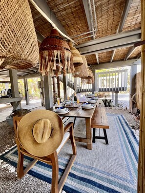 An outdoor dining area with a wooden table set for two, surrounded by woven baskets and a straw hat on a chair. - Santa Clara: Modern 3BR Harborfront Retreat with Safety Harbor Club Access (Captiva)