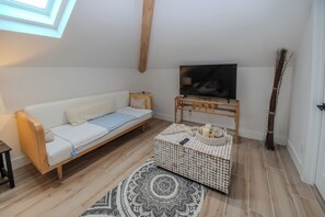A modern living room with a sofa, a television on a wooden stand, a patterned ottoman, and a large window. - Santa Clara: Modern 3BR Harborfront Retreat with Safety Harbor Club Access (Captiva)