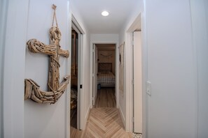 Ein Flur mit Holzboden, einer an der Wand befestigten Kletterskulptur und einem Bett mit gemustertem Überwurf im Hintergrund.