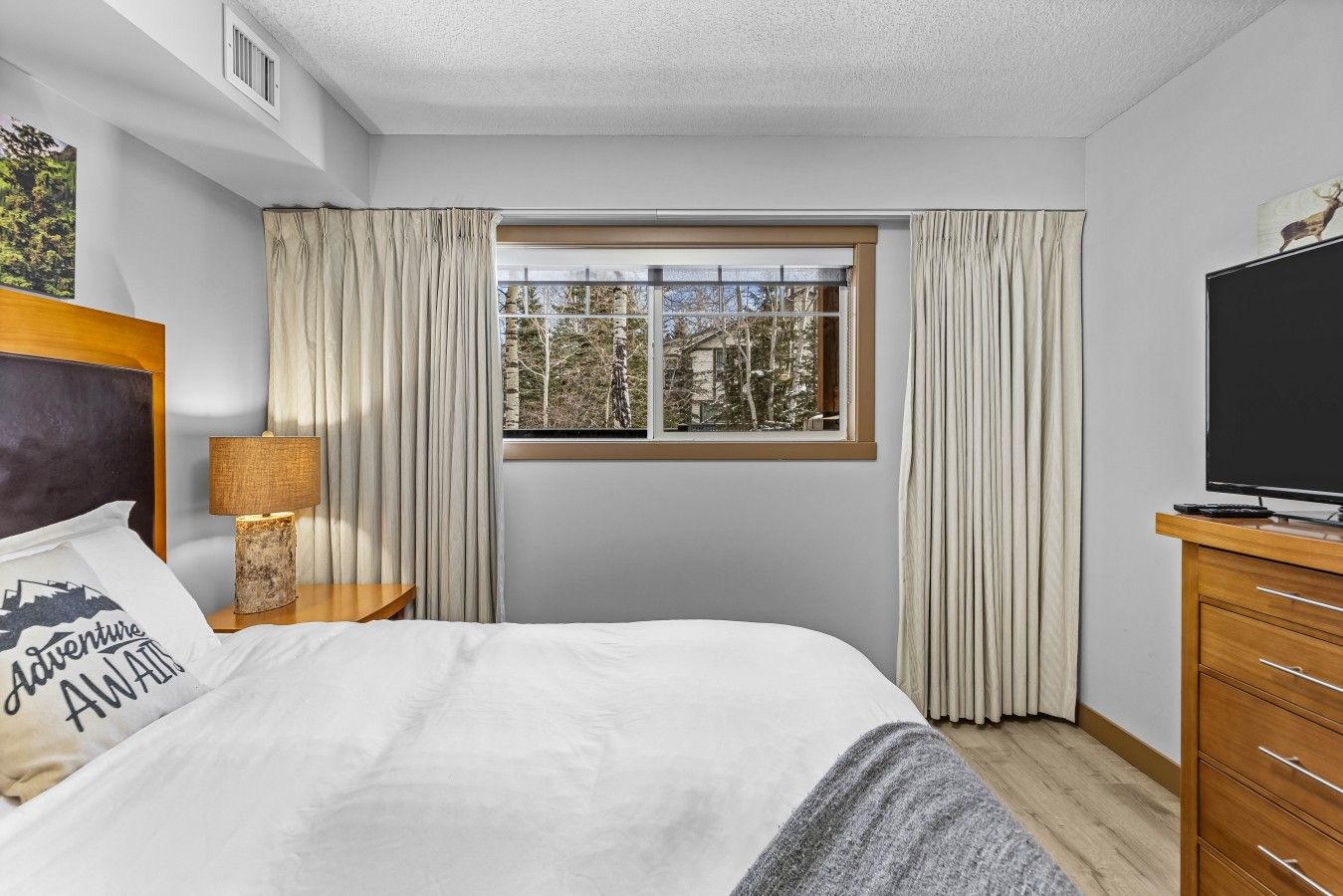 Een hotelkamer met een bed, een televisie, een raam met gordijnen en een lamp.