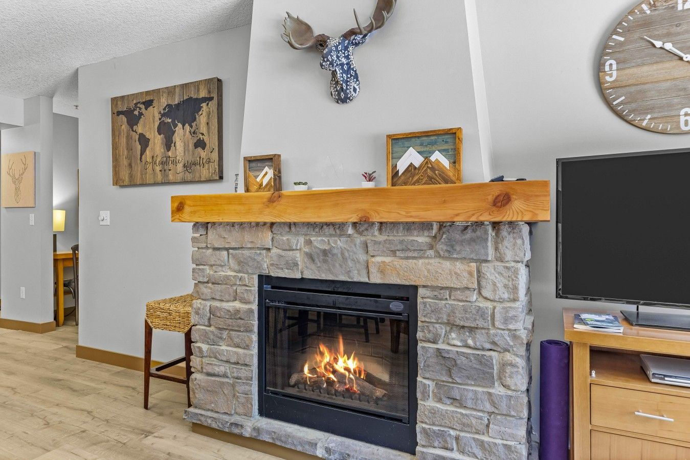 Un salon avec une cheminée en pierre, une tête de cerf accrochée au mur, une carte du monde et un téléviseur.