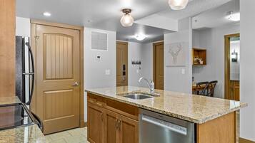 A modern kitchen with granite countertops, stainless steel appliances, wooden cabinets, and pendant lighting.