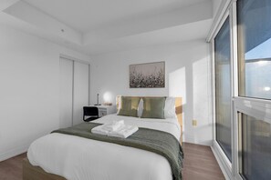 Quarto com cama, mesa de cabeceira, cadeira, janela e um quadro na parede.
