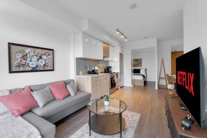 A modern living space with a sofa, coffee table, flat-screen TV, and a kitchen area. - Heart of Downtown - 2BR - Near Dundas Square (Toronto)