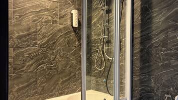 A modern bathroom with a glass-enclosed shower, a white bathtub, and dark marble walls.