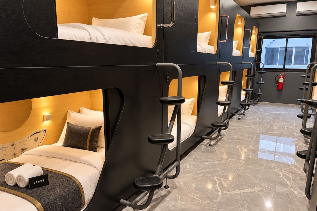 A row of bunk beds with attached exercise equipment, a fire extinguisher, and a window with a view.