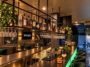 Una zona de bar con una variedad de botellas de licores, una pantalla de televisión y taburetes.