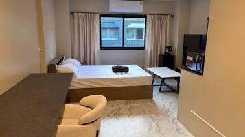 A hotel room with a bed, a desk, a chair, a television, and a window with curtains.