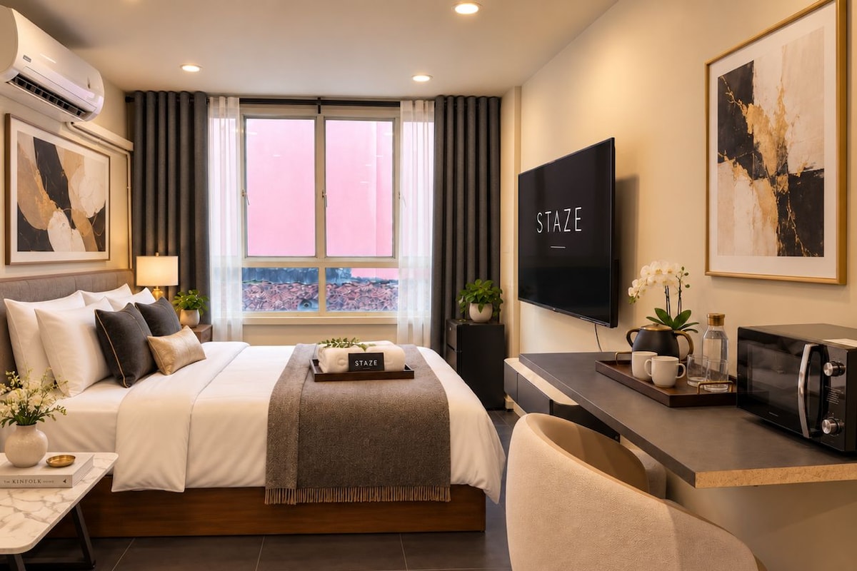 A modern hotel room with a bed, a desk, a television, and a window with curtains.